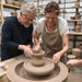 A teacher showing a pupil how to use a pottery wheel